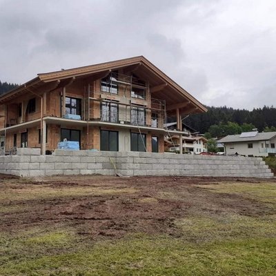 Moderne Gartenmauer in Natursteinoptik stützt das Gelände und ergänzt den Neubau harmonisch