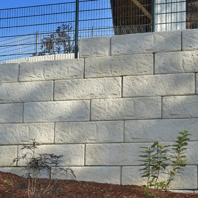 Helle Betonmauer mit Zaun schützt das höher liegende Grundstück zuverlässig