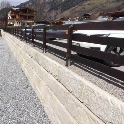 Gerade verlaufende Beton-Stützwand mit Holzzaun sichert das Parkplatzniveau im Hangbereich