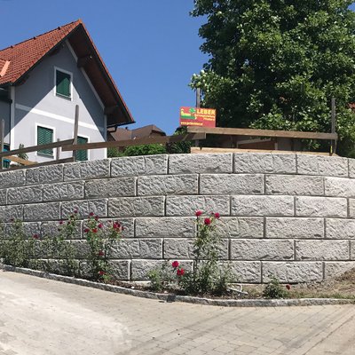 Halbkreisförmige Gartenmauer mit strukturierter Oberfläche und rosigem Beet davor